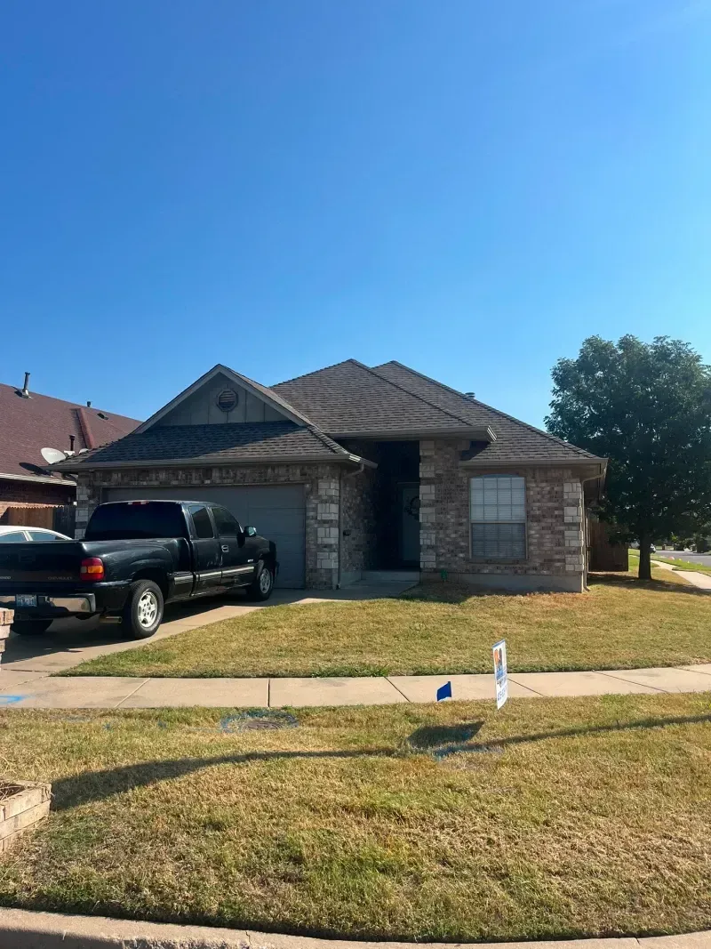 House with brown tile roof, brick exterior, and a black truck parked in the driveway on a sunny day.