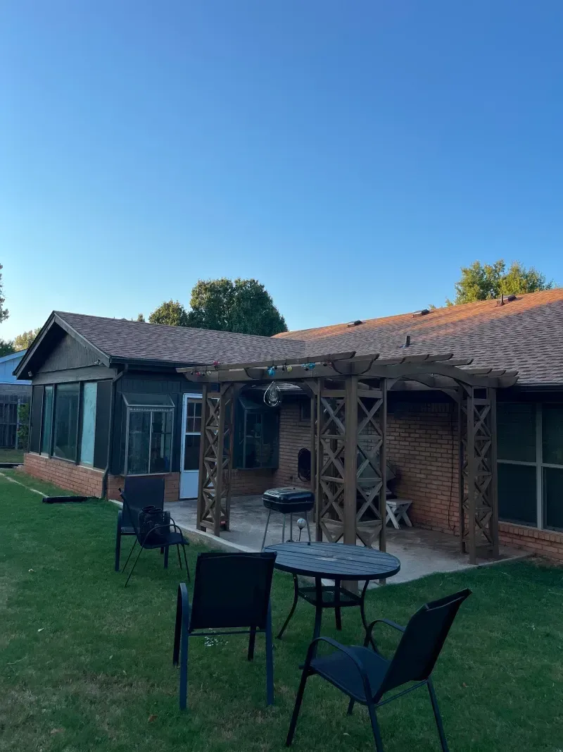 Backyard patio with a pergola, brick house, and lawn furniture.
