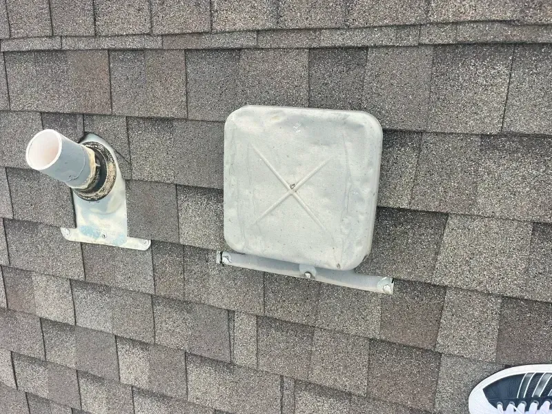 Close-up of a roof with two ventilation components, a white pipe, and a square metal cap.