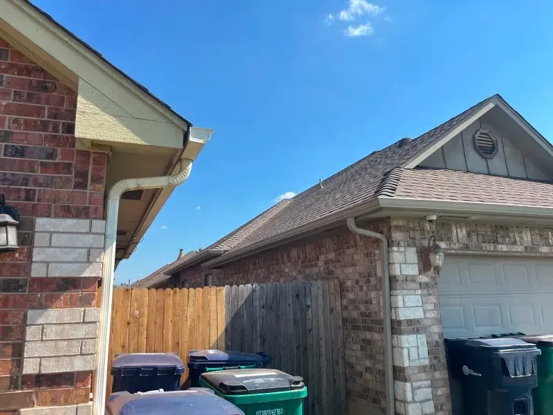 Two brick houses with gutters, blue sky, trash cans, and wooden fence.