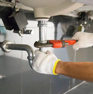 Plumber fixing white sink pipe with adjustable wrench.