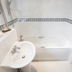 A general view of a bathroom with white suite and glass shower screen, with scented sticks, a lit candle and a bar of soap sitting on a shelf.