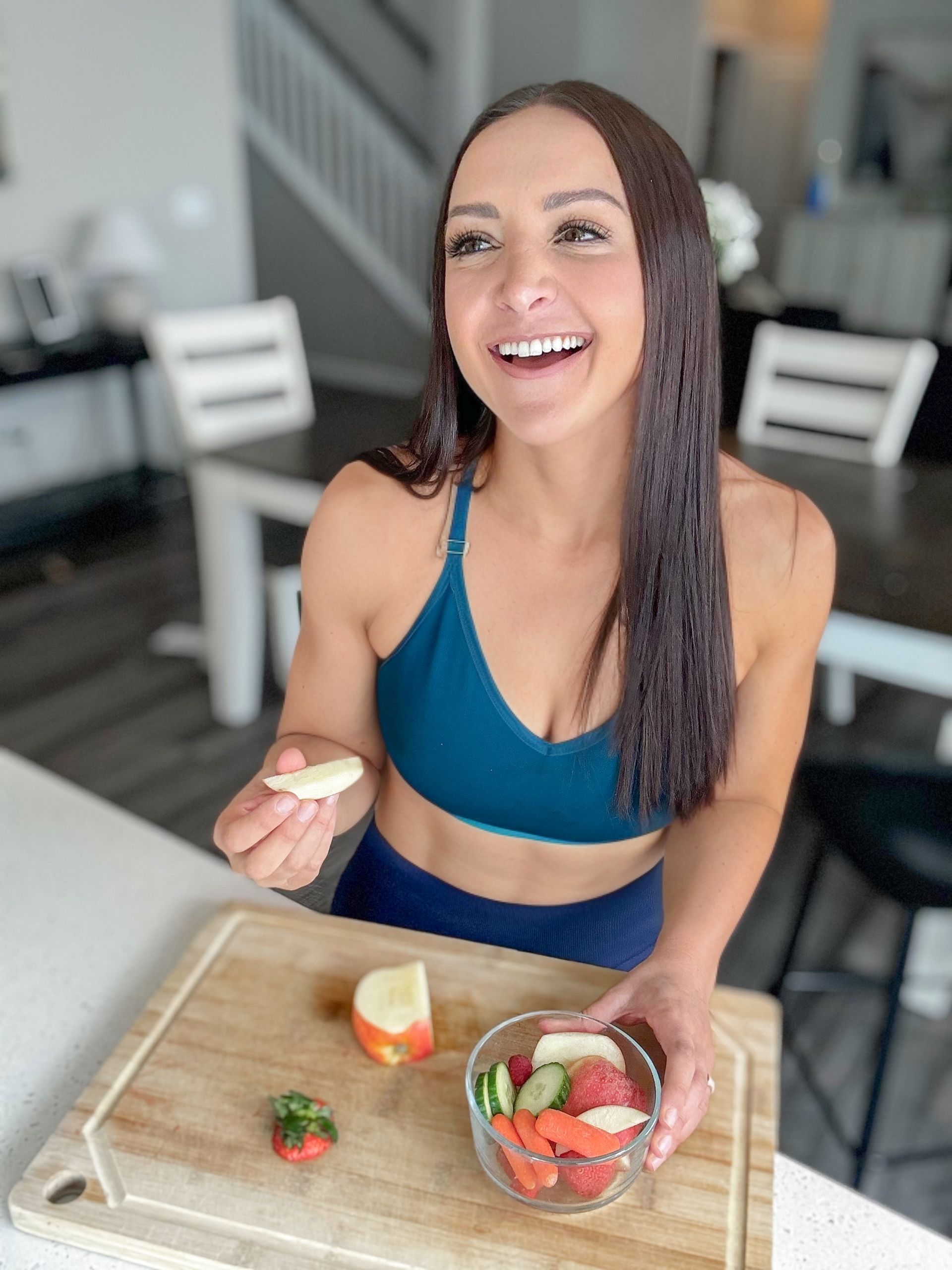 A woman is sitting at a table with a bowl of fruit and a cutting board.  Alyssa Favreau - Switch 2 Strength