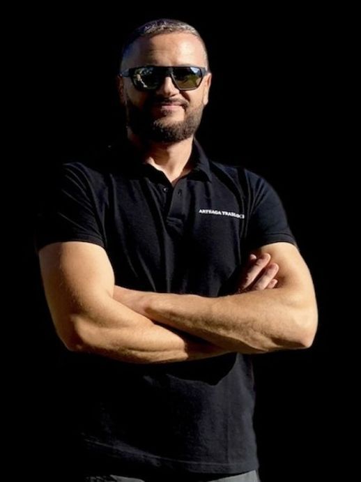 Un uomo che indossa occhiali da sole e una camicia nera è in piedi con le braccia incrociate.