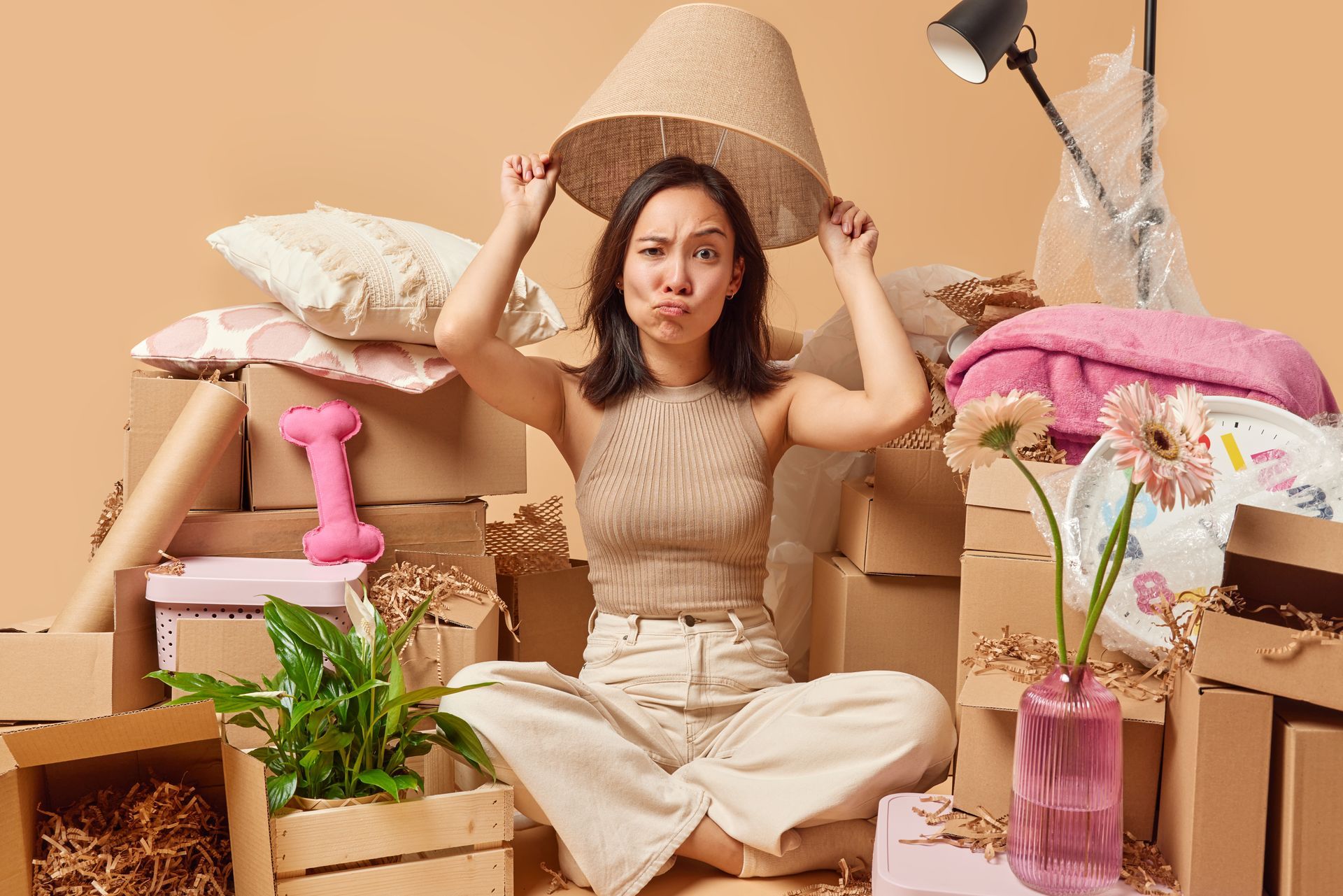 A woman is sitting on the floor with a lamp on her head surrounded by cardboard boxes.
