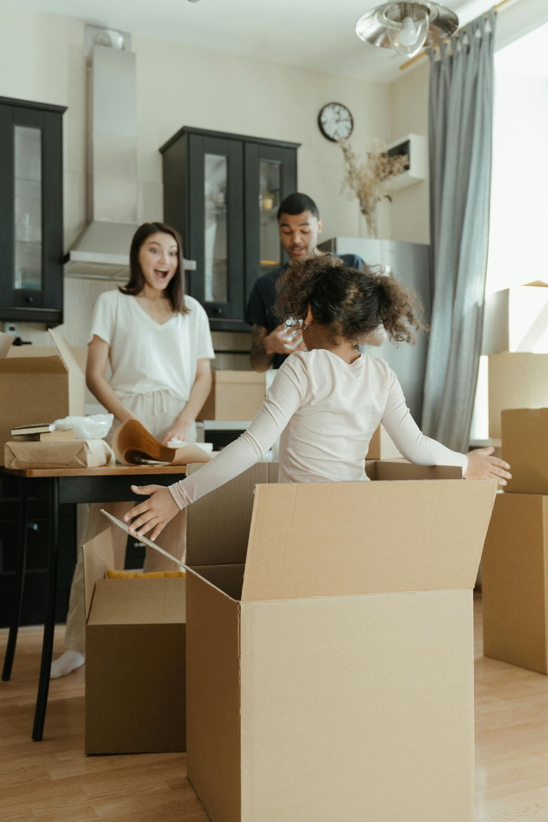 A family is moving into a new home and a little girl is sitting in a cardboard box.
