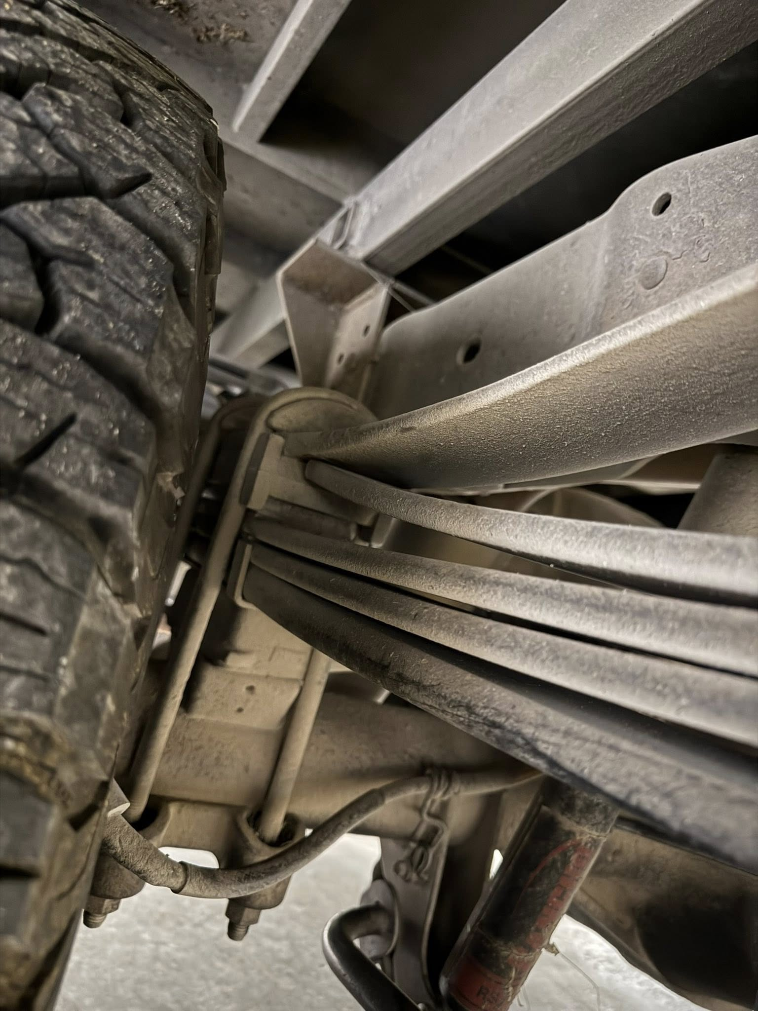 Undercarriage of a vehicle with a tire, leaf springs, and suspension components visible.