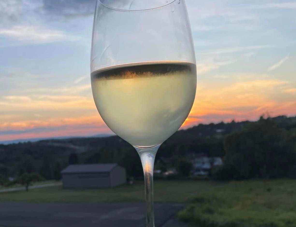 A close up of a glass of wine with a sunset in the background.