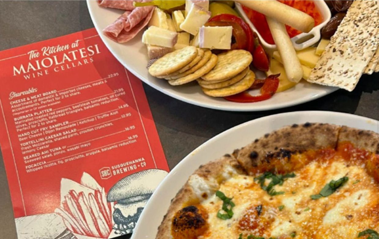 A pizza and a plate of food are on a table next to the Maiolatesi Kitchen menu.