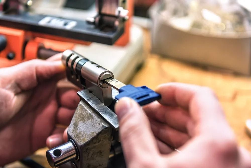 Hands Holding a Key and a Lock Cylinder in a Vise, Locksmithing Equipment — CTS Locksmiths in Maroochydore, QLD