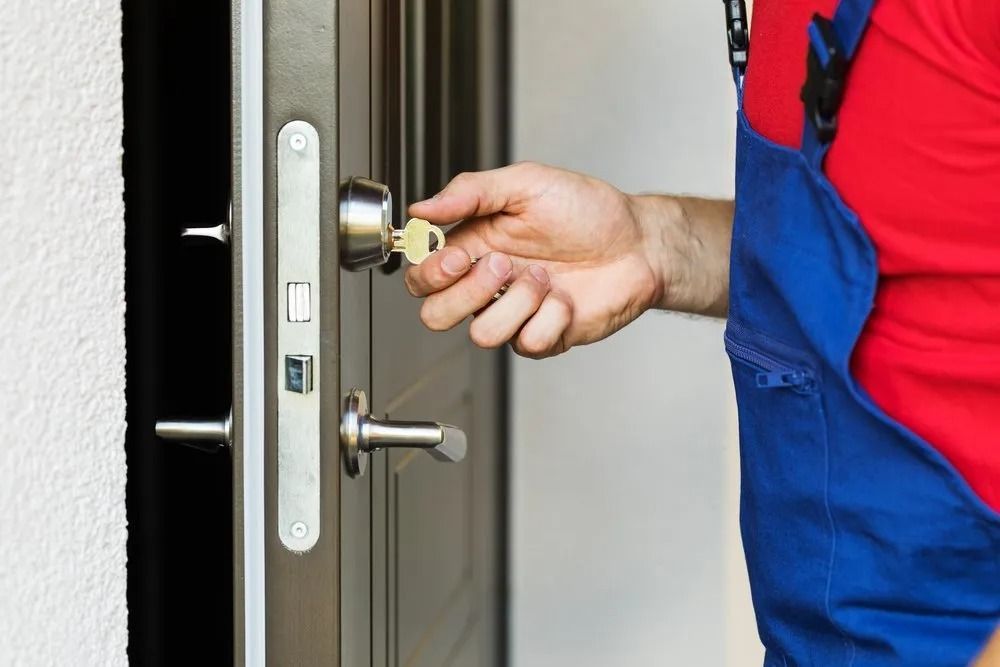 Hand of Person in Blue Overalls Inserting Key Into a Dark Door Lock — CTS Locksmiths in Maroochydore, QLD