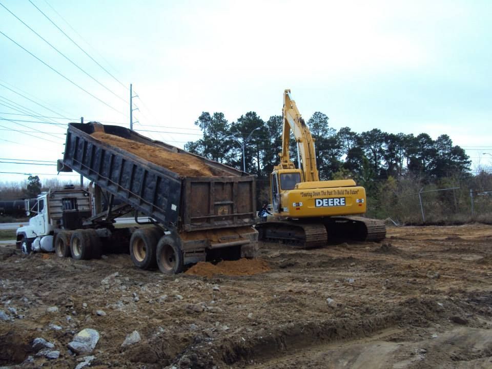 Excavator dumping soil into a dump truck on a construction site.