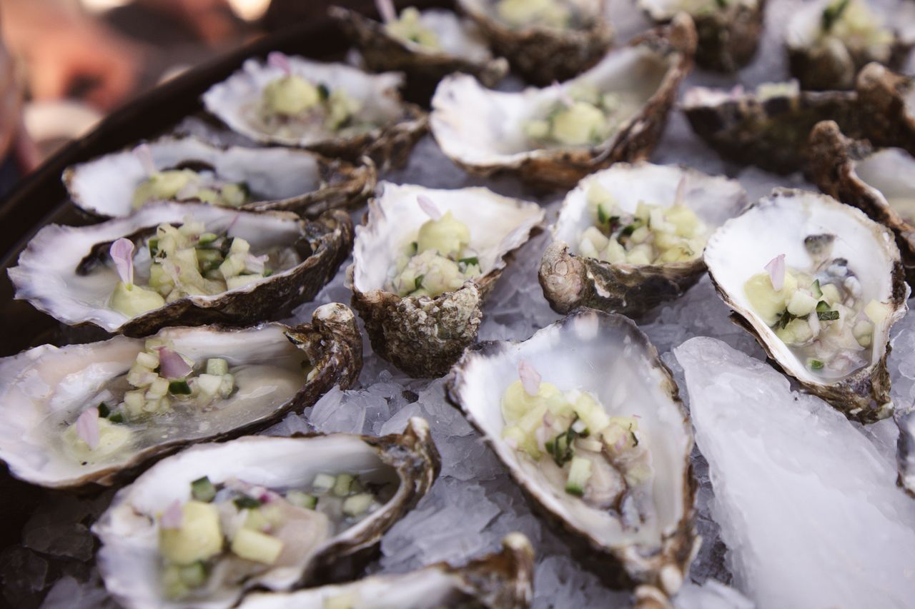 Oesters op ijs, gegarneerd met fijngehakte groenten, gepresenteerd op een dienblad.