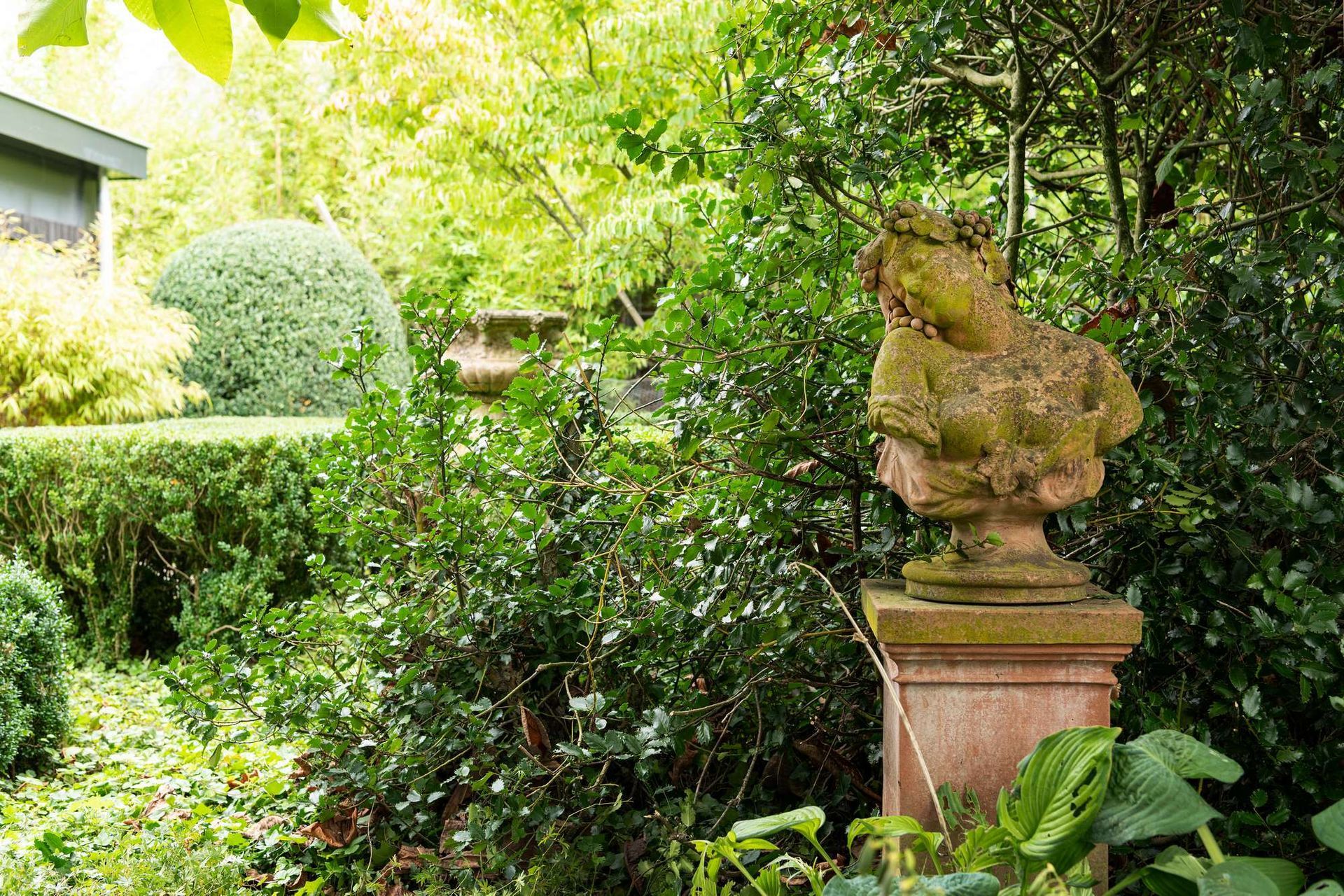 Stenen buste in een verwilderde tuin.