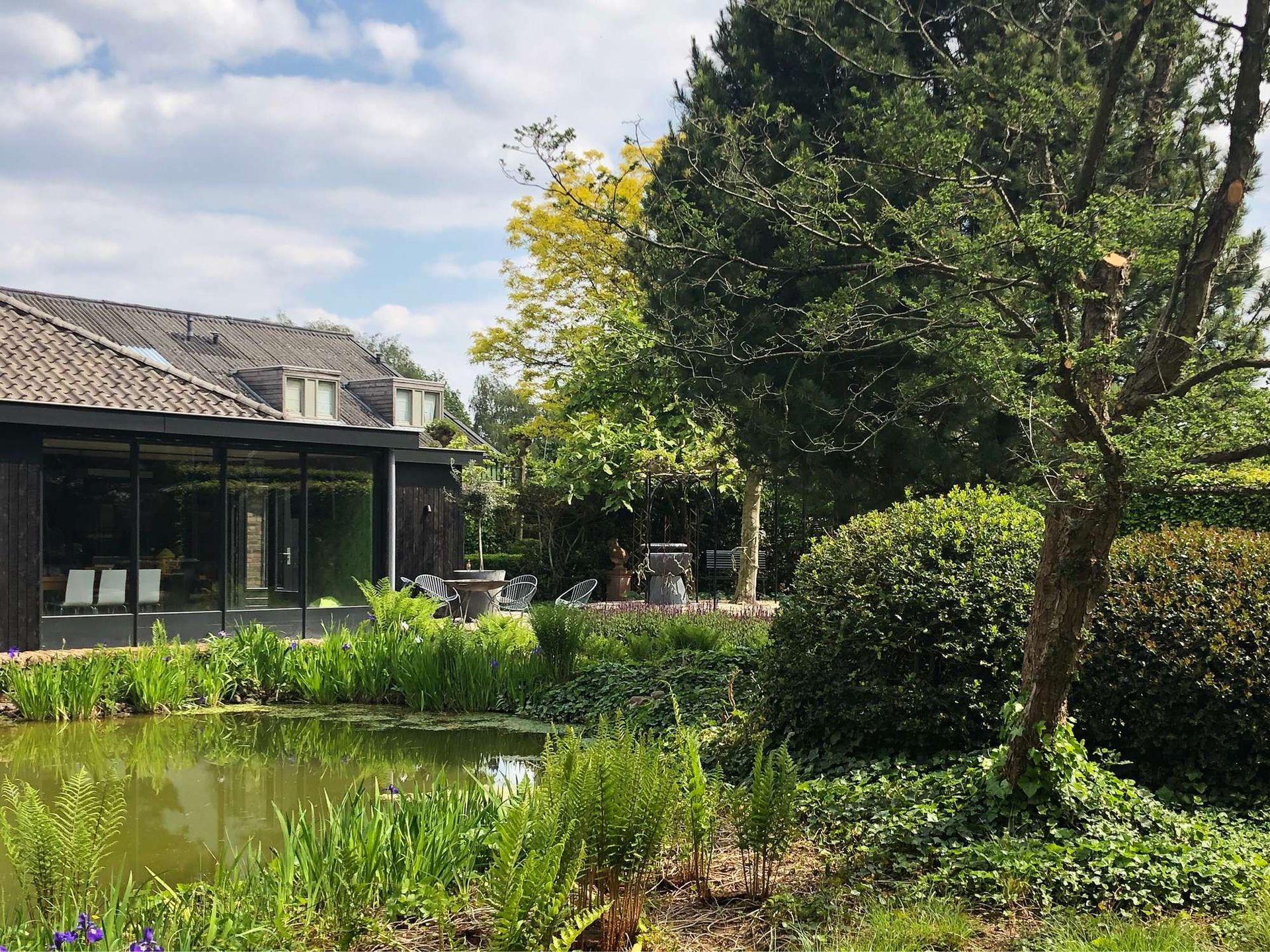 Een vijver in een tuin met een modern gebouw en weelderig groen op een zonnige dag.