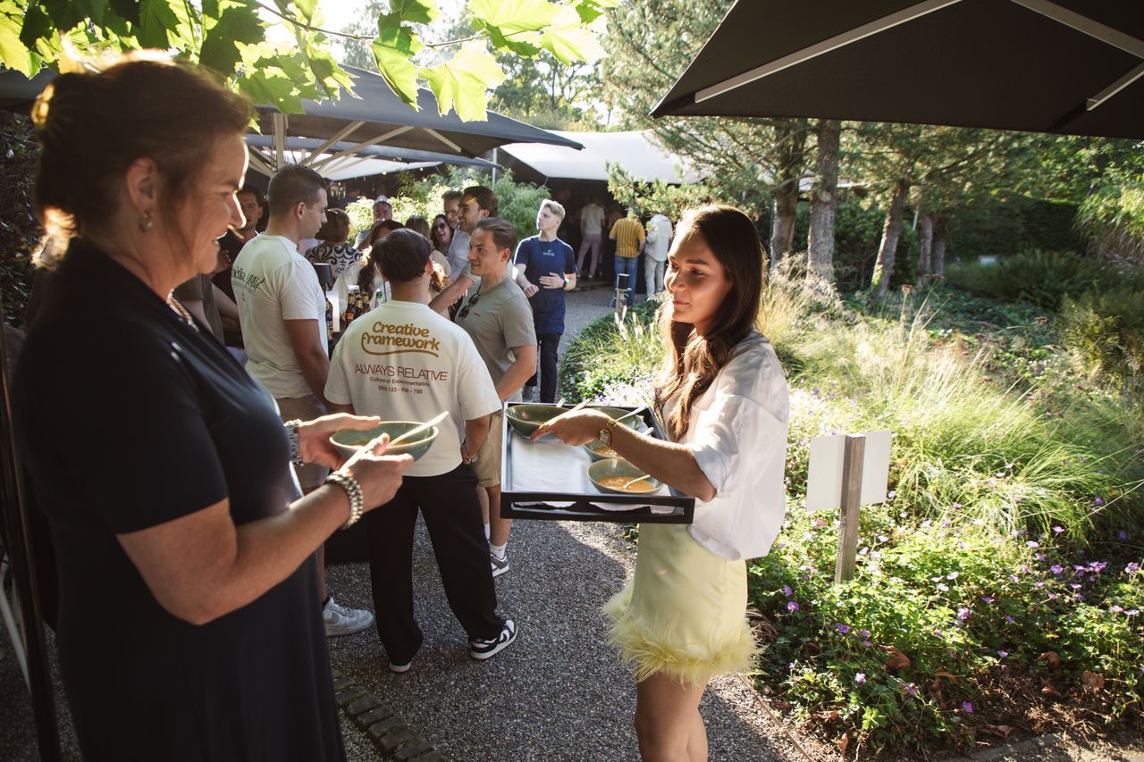 Vrouw betaalt, ober houdt dienblad vast, buitenevenement met andere aanwezigen in de zon.