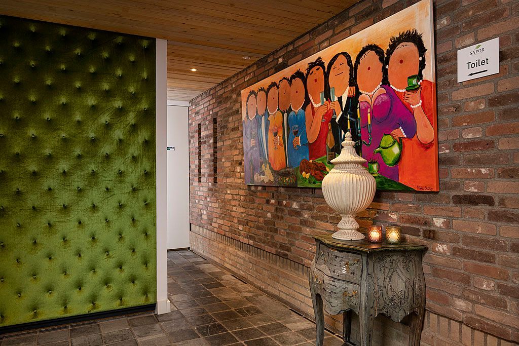 Hal met bakstenen muur, groot schilderij, groene fluwelen lambrisering en een decoratieve tafel.