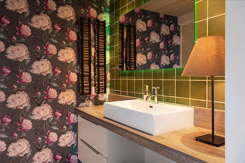 Badkamer met bloemenbehang, witte wastafel, groene tegels en een lamp.