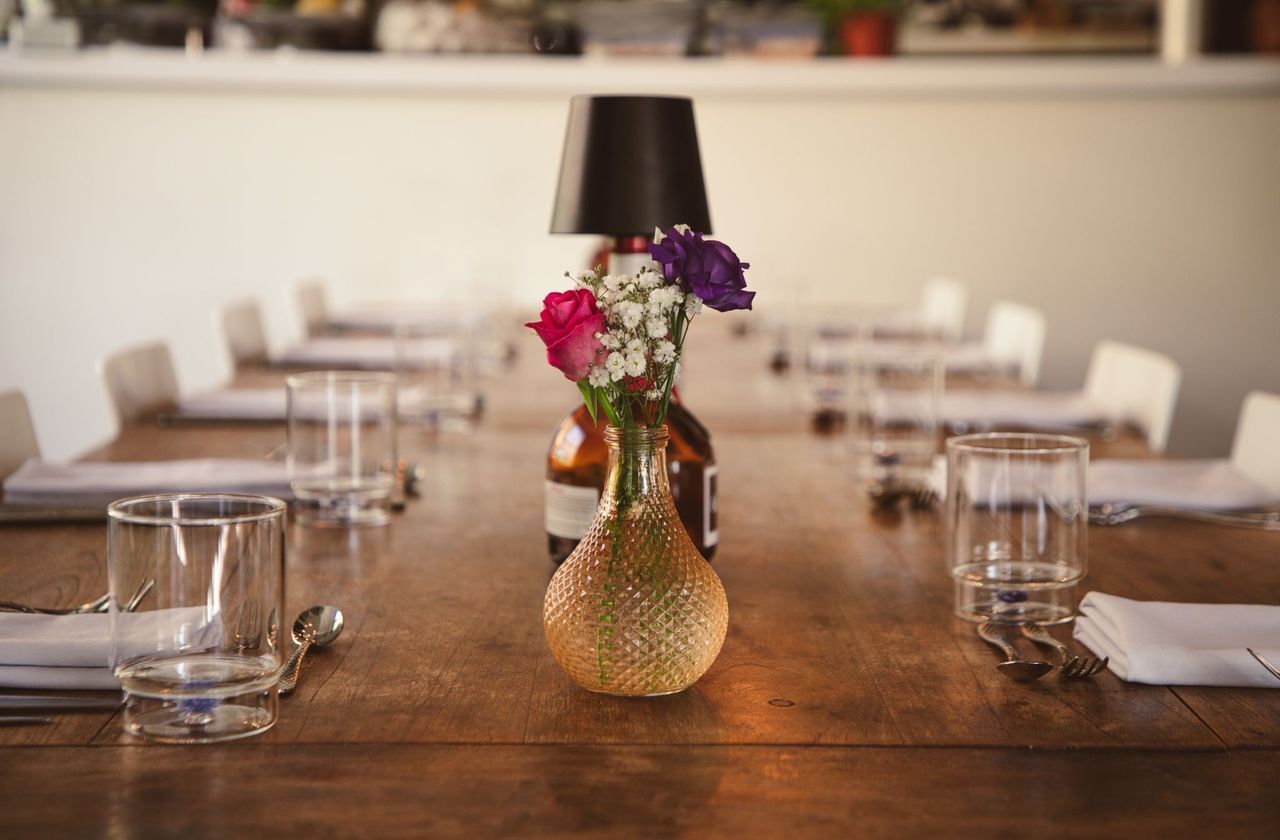 Een lange houten eettafel, gedekt voor gasten met bloemen, glazen en tafelkleden.