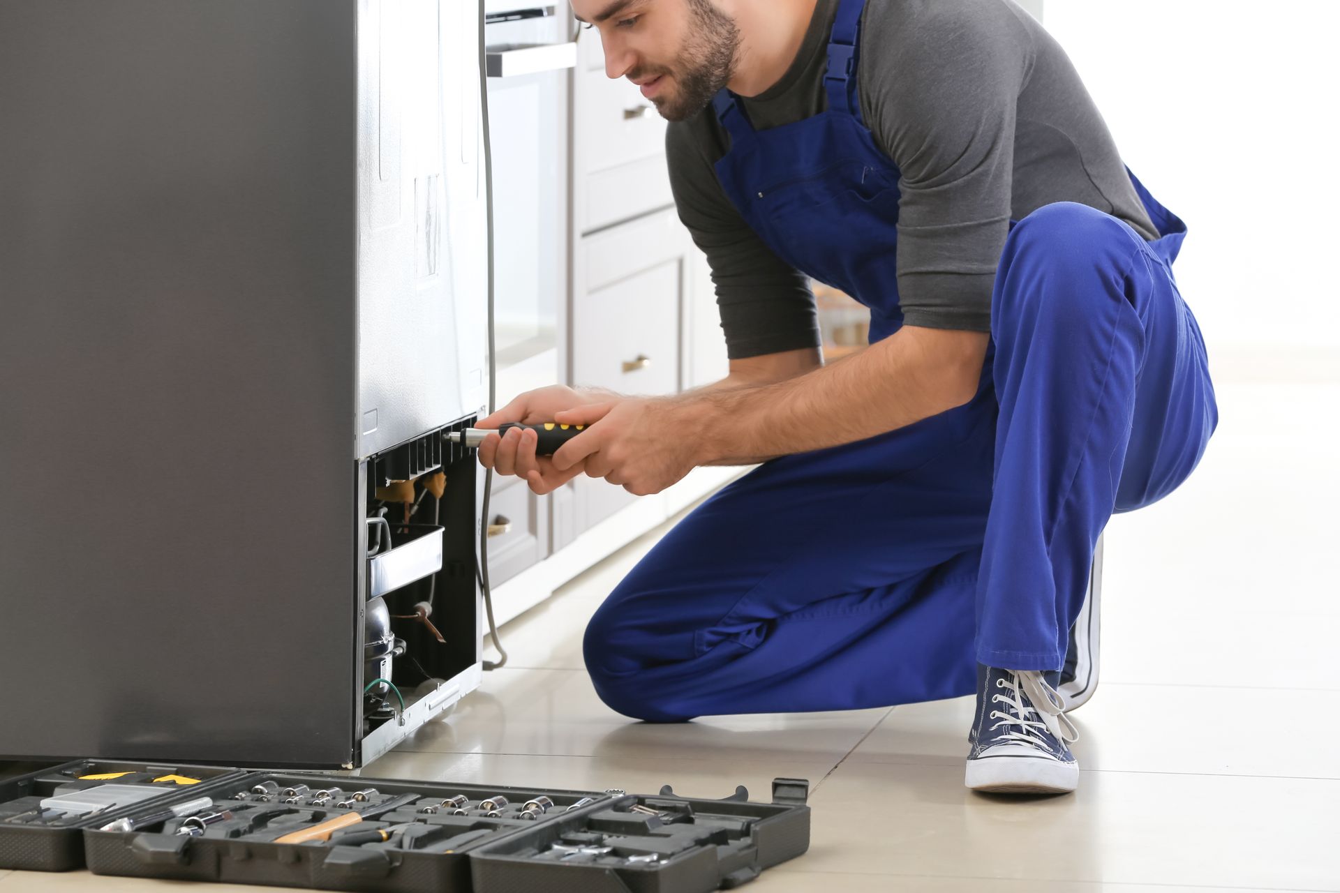 An appliance repair technician servicing a household refrigerator with professional tools.