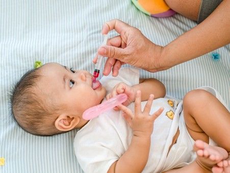 Infant being safely administered liquid medicine by an adult using an oral dosing syringe.