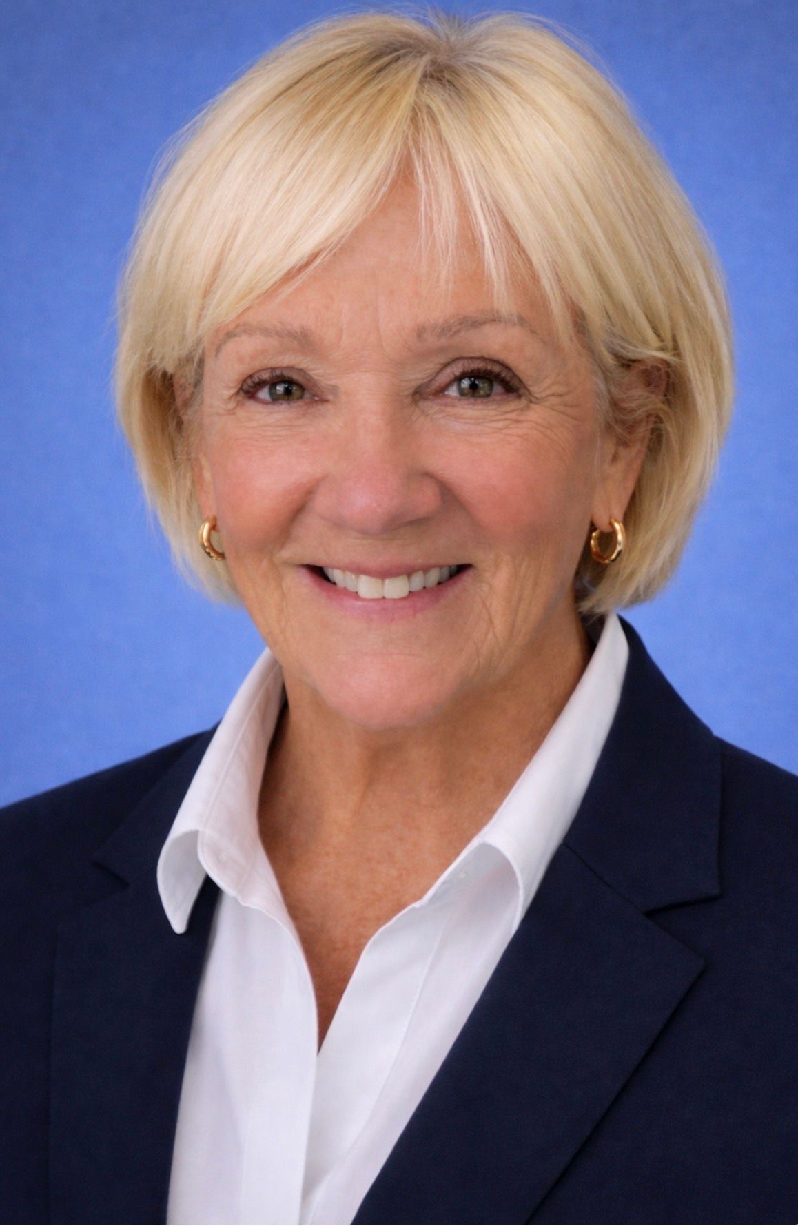 A woman with red hair and pearl earrings is smiling for the camera.