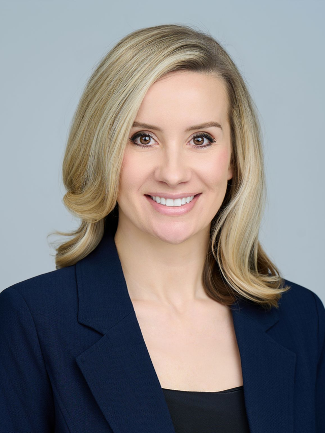 Professional headshot of a smiling person in a navy blazer against a light gray background