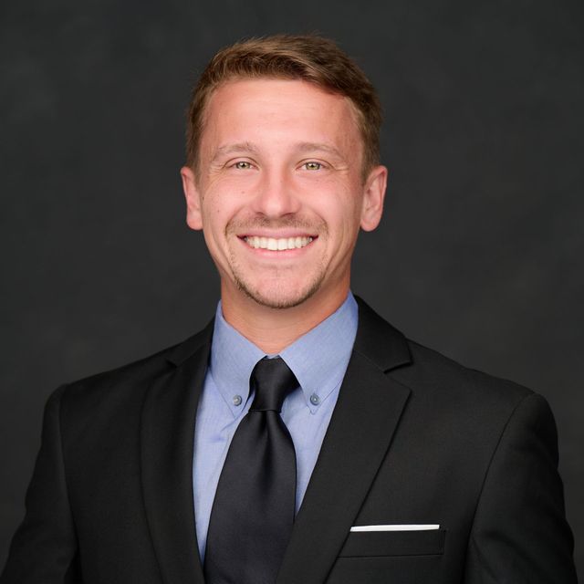 Smiling man in a black suit and tie against a dark background