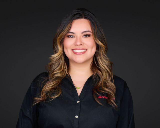 Smiling person with wavy hair in a black shirt against a dark gray background