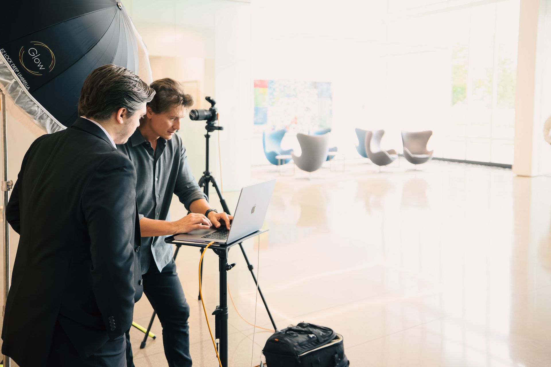 Two men are standing next to each other in front of a laptop computer.