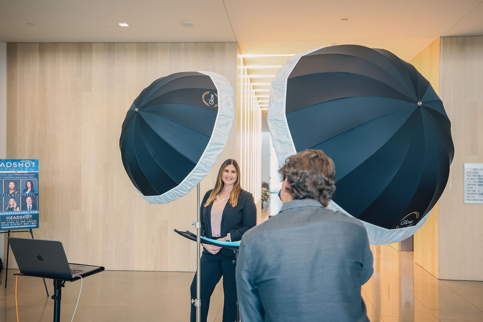 A man is taking a picture of a woman standing in front of two umbrellas.