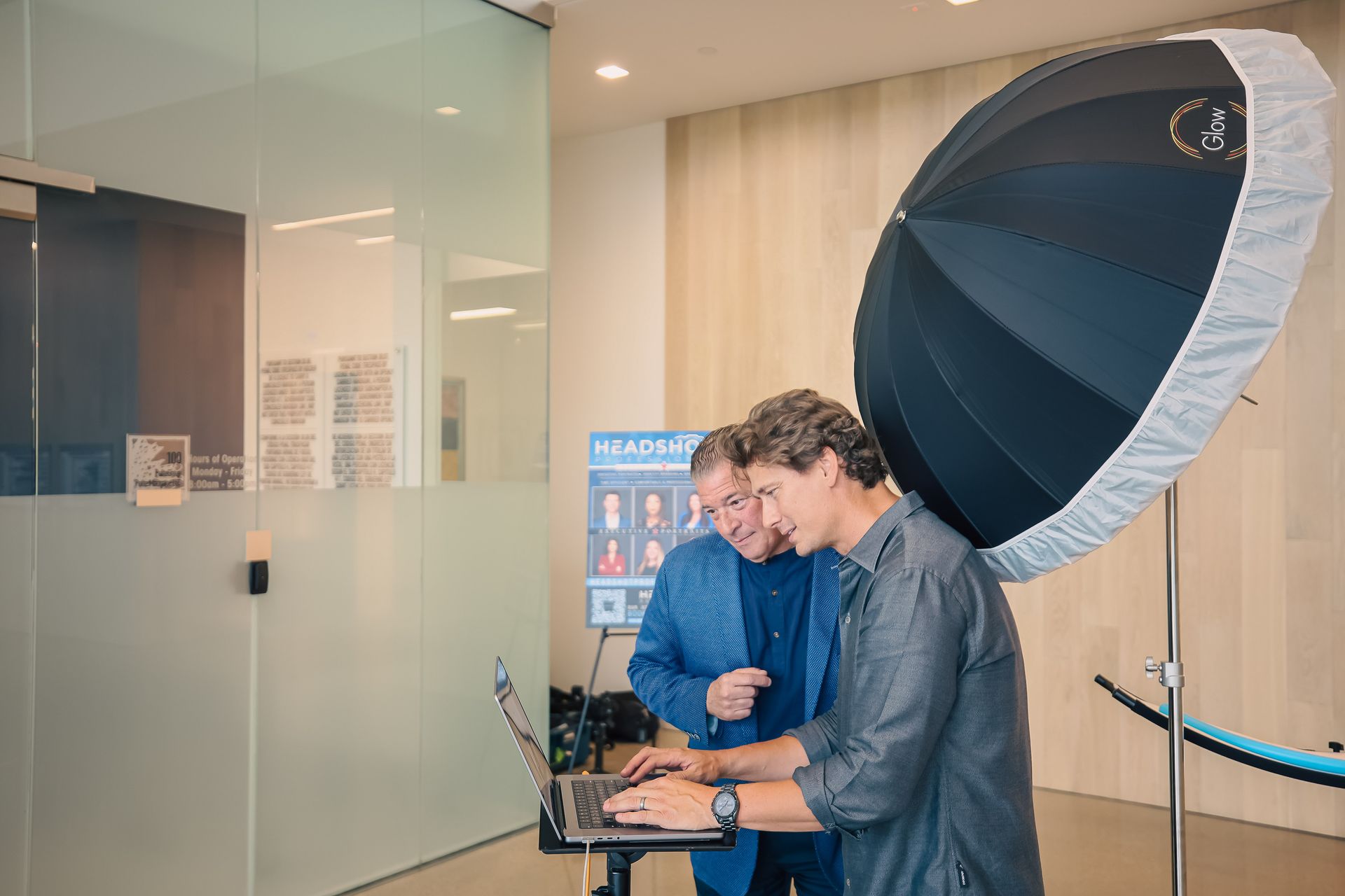 Two men are standing next to each other in a room looking at a laptop.