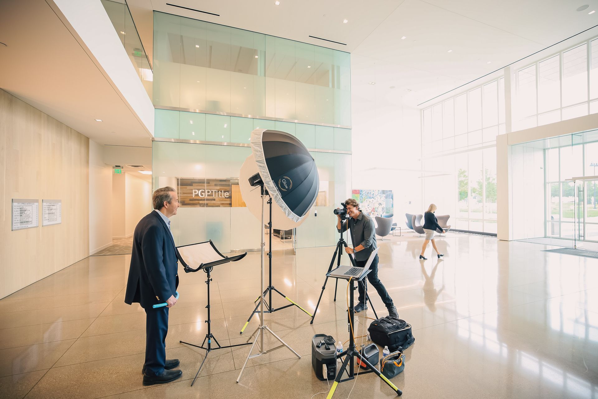 A man in a suit is standing in front of a camera in a lobby.