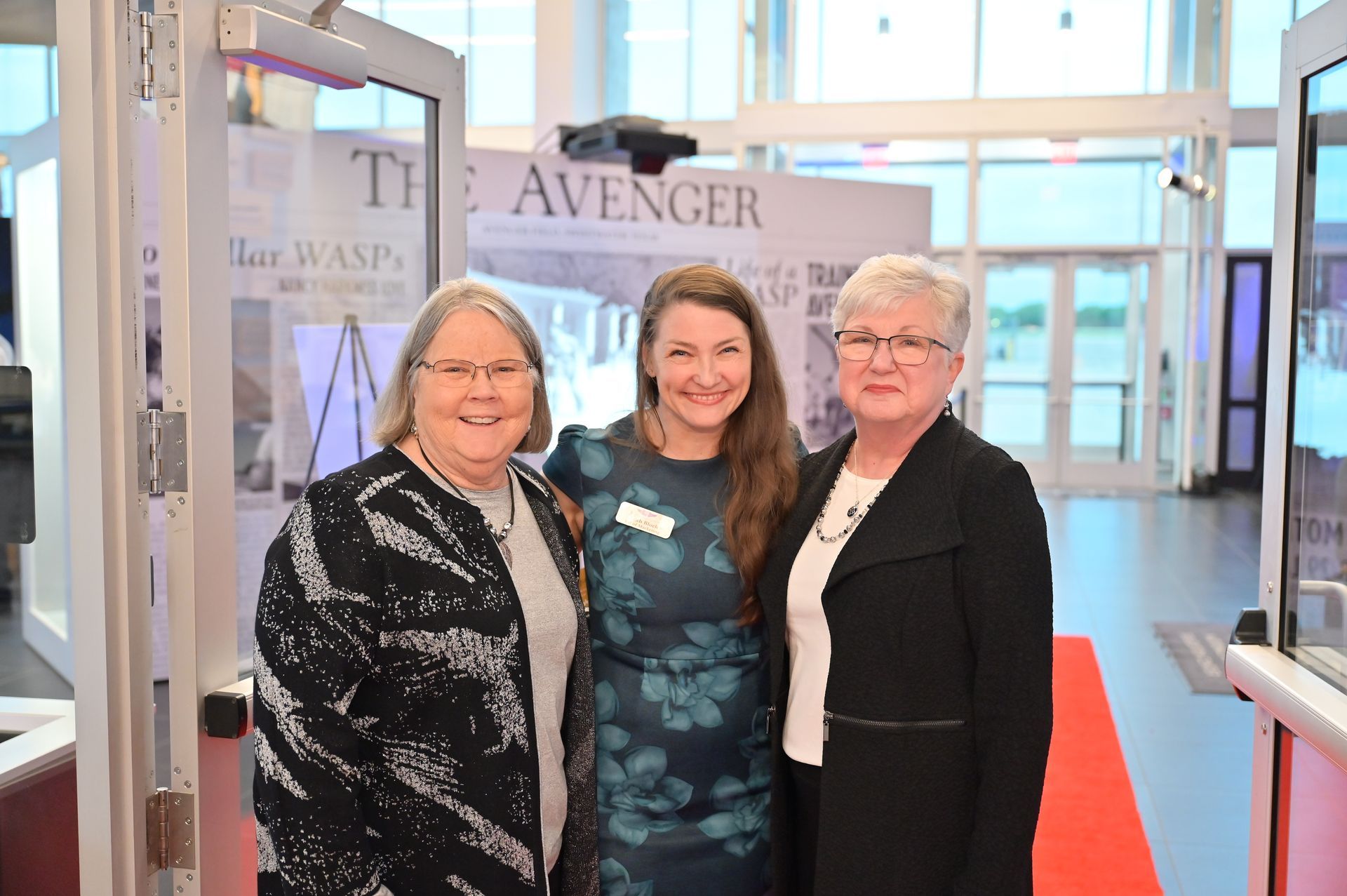 Three women are standing next to each other on a red carpet.