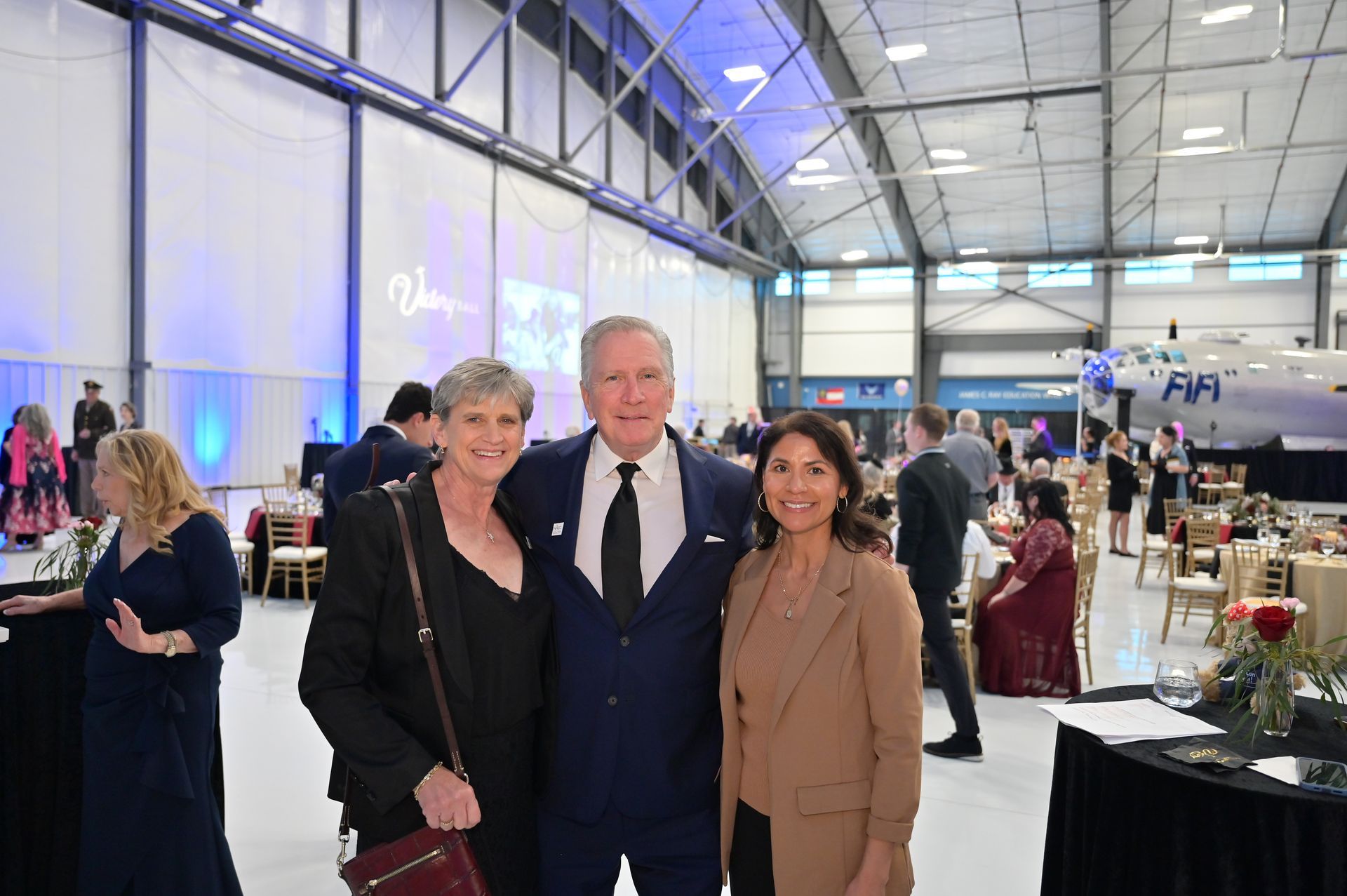A man and two women are posing for a picture in a large room.