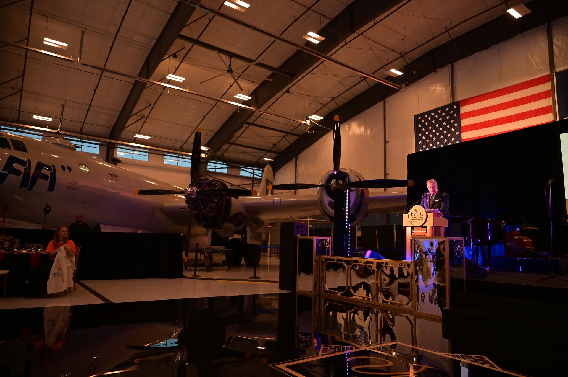 A man is giving a speech in front of an airplane in a hangar.