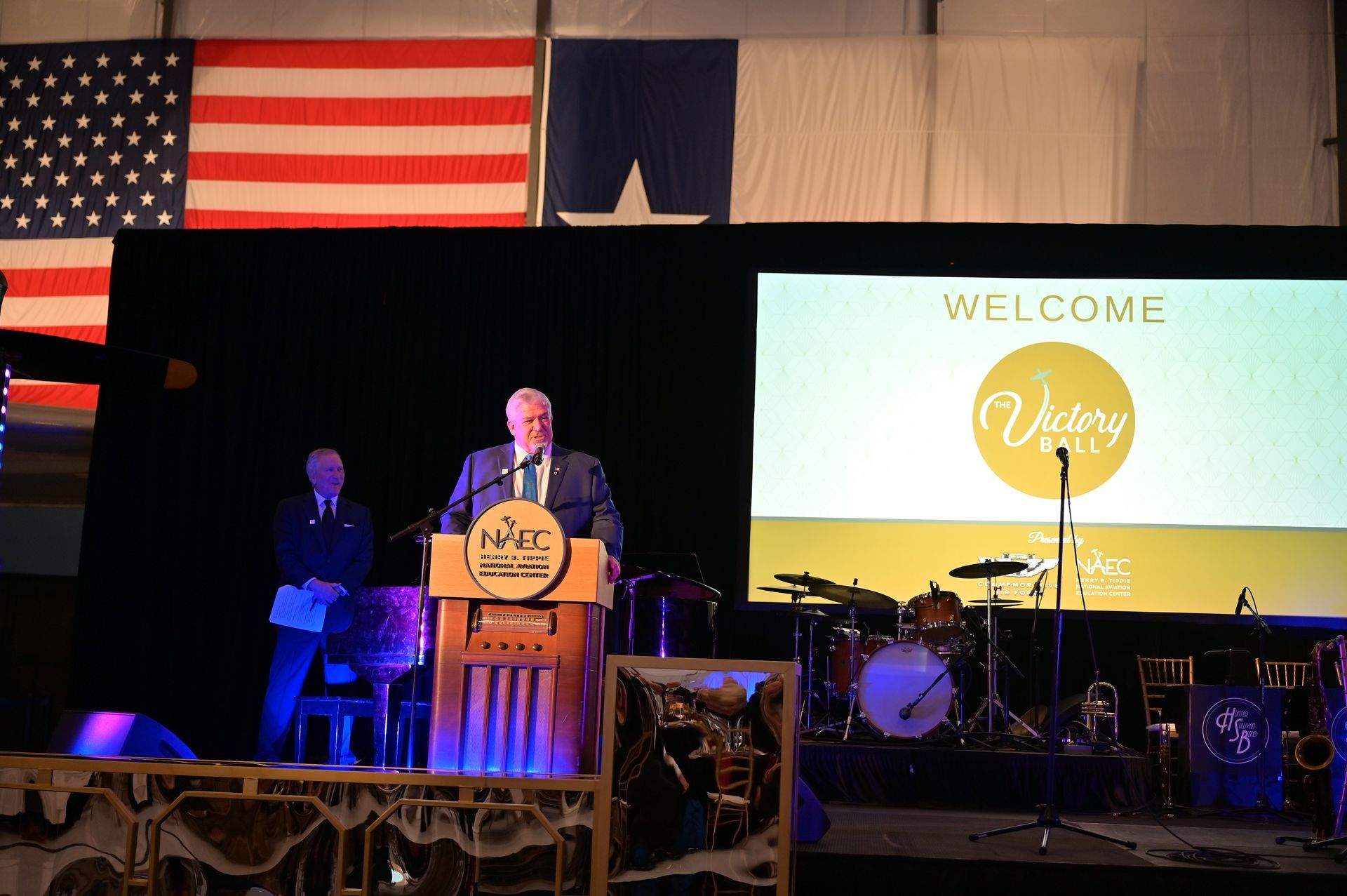 A man stands at a podium in front of a large screen that says welcome