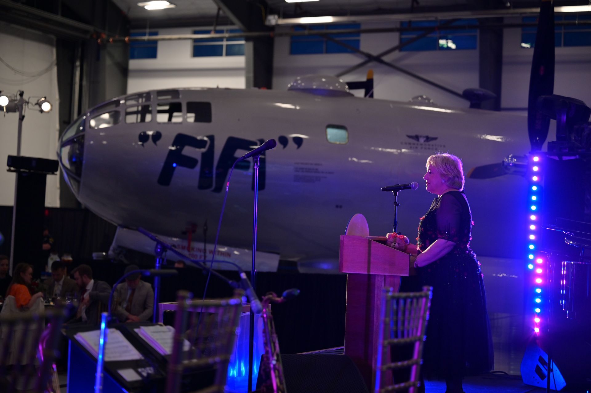 A woman stands at a podium in front of an airplane that says fif