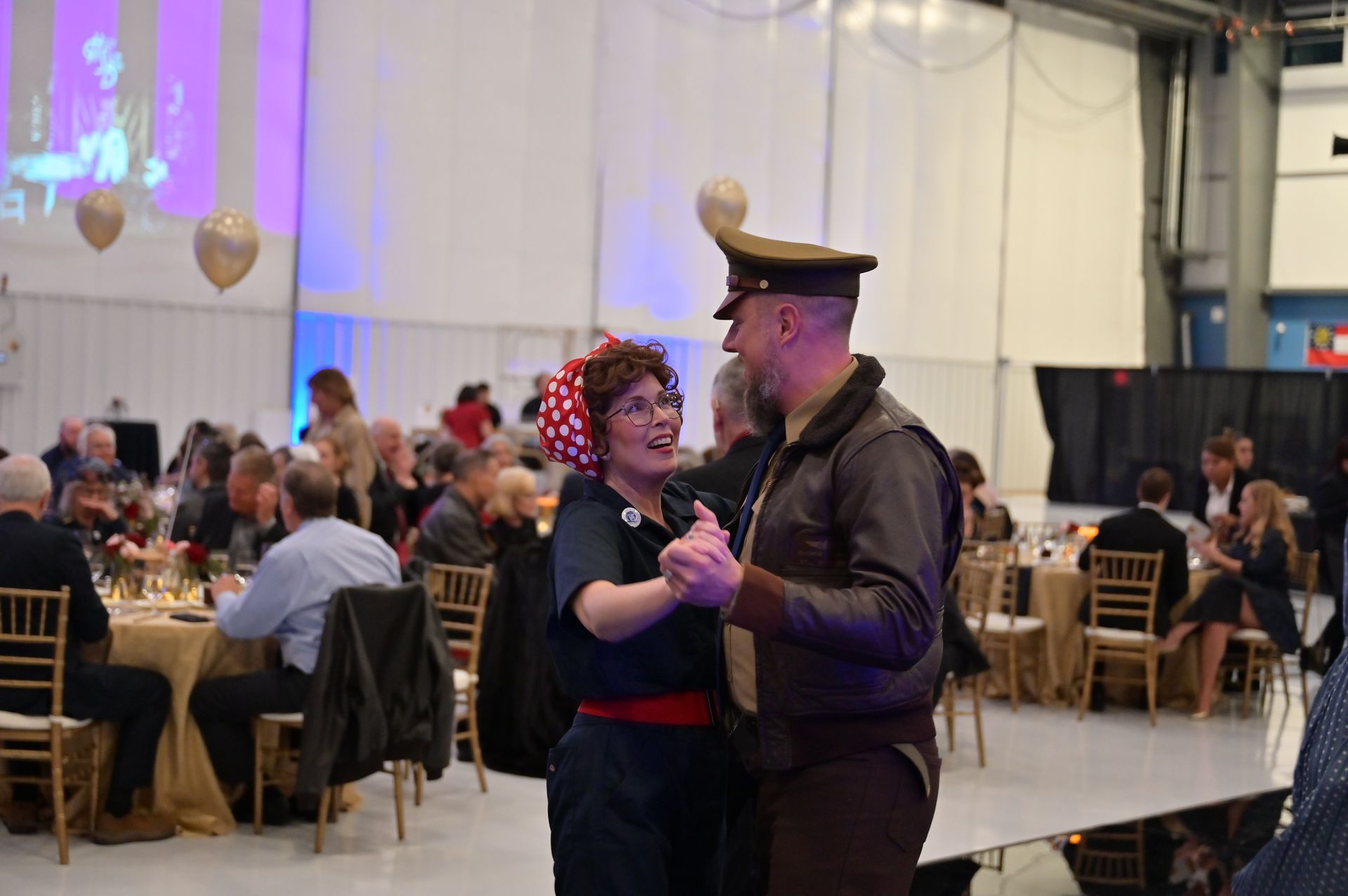 A man and a woman are dancing in a room with people sitting at tables.