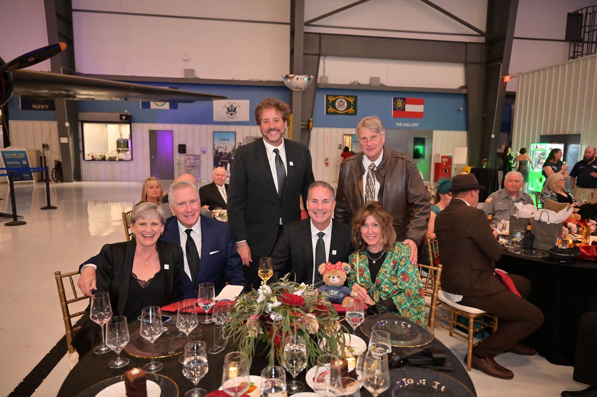 A group of people are posing for a picture at a table with wine glasses.