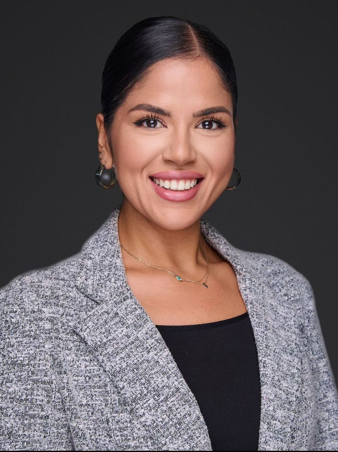 A woman wearing a gray jacket and a black shirt is smiling for the camera.