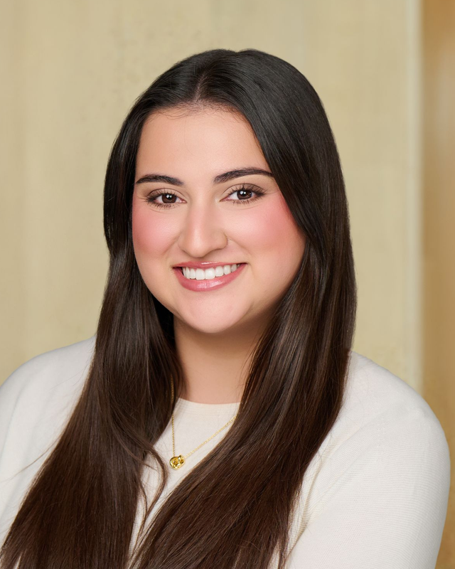 Smiling woman with long dark hair wearing a white top against a beige background