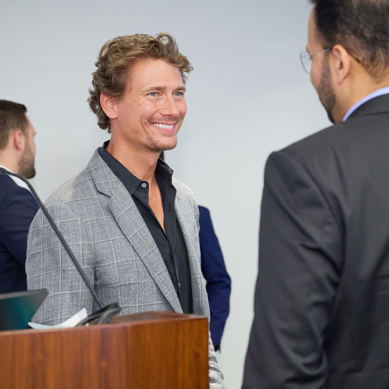 A man in a suit stands at a podium talking to another man