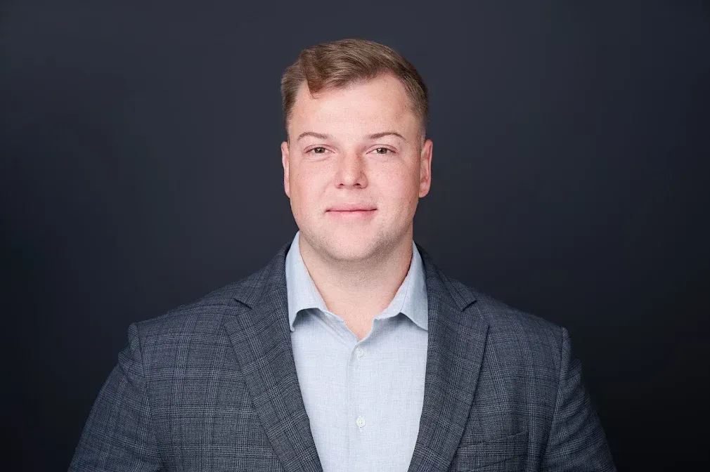 A man in a suit and white shirt is standing in front of a black background.