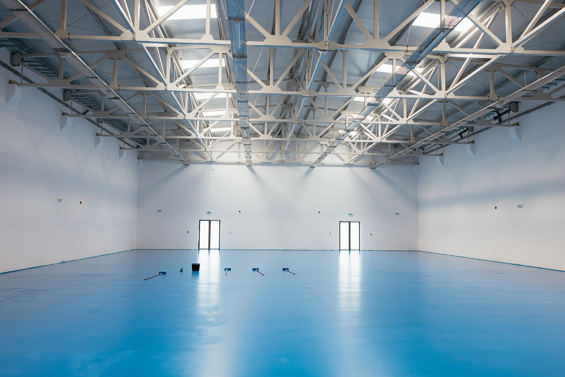 Empty blue-floored warehouse with white walls and exposed ceiling beams