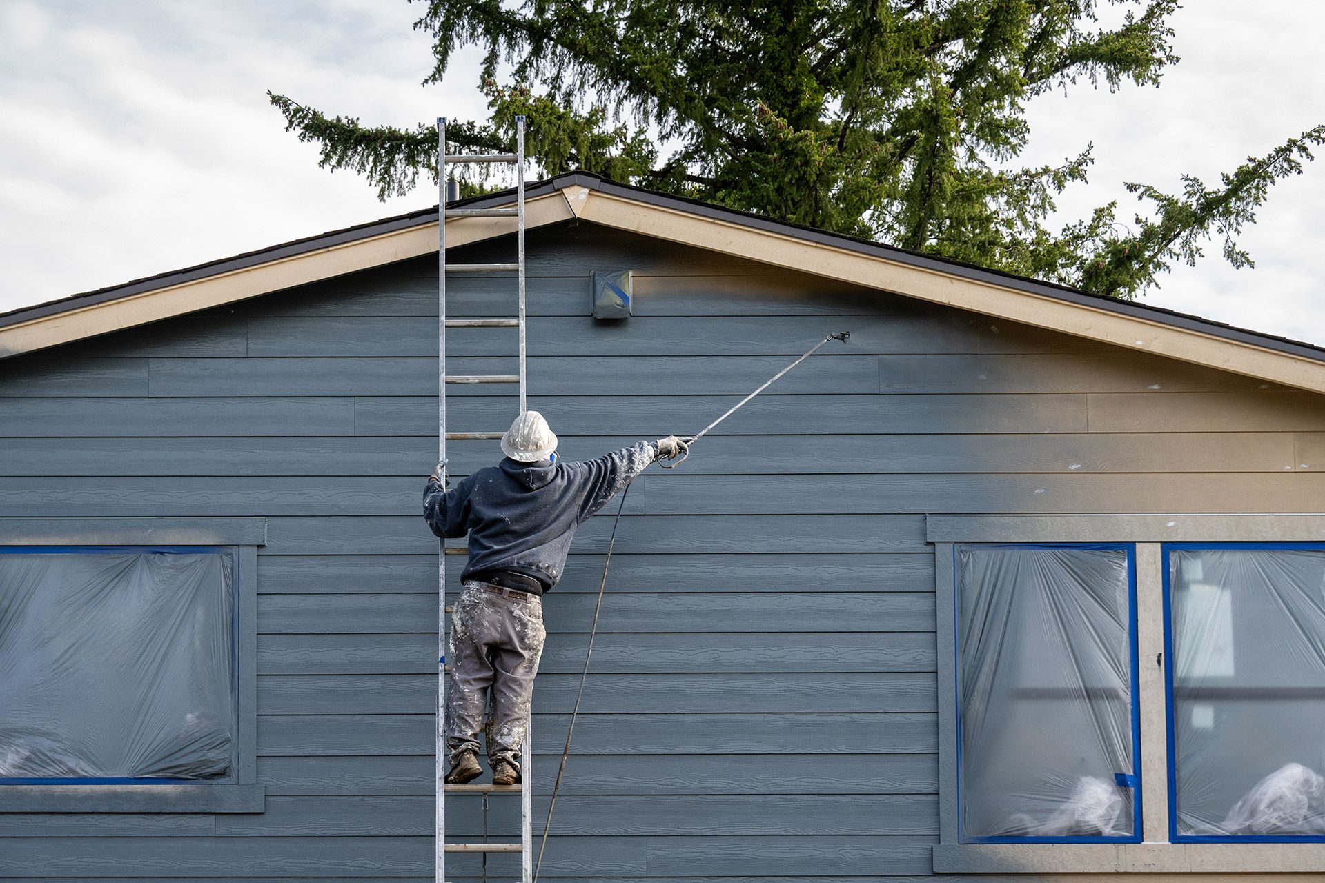 Person on a ladder painting the blue exterior of a house with a roller