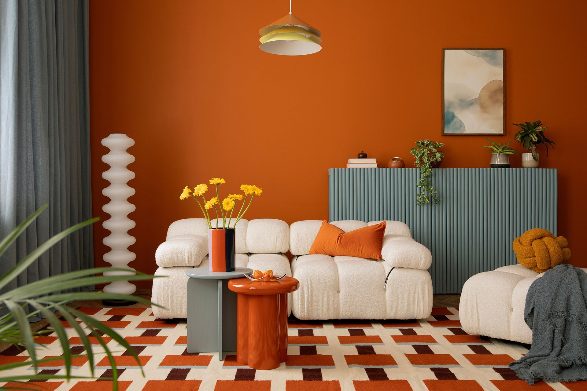 Orange-and-white living room with a white sofa, patterned rug, plants, and modern decor.
