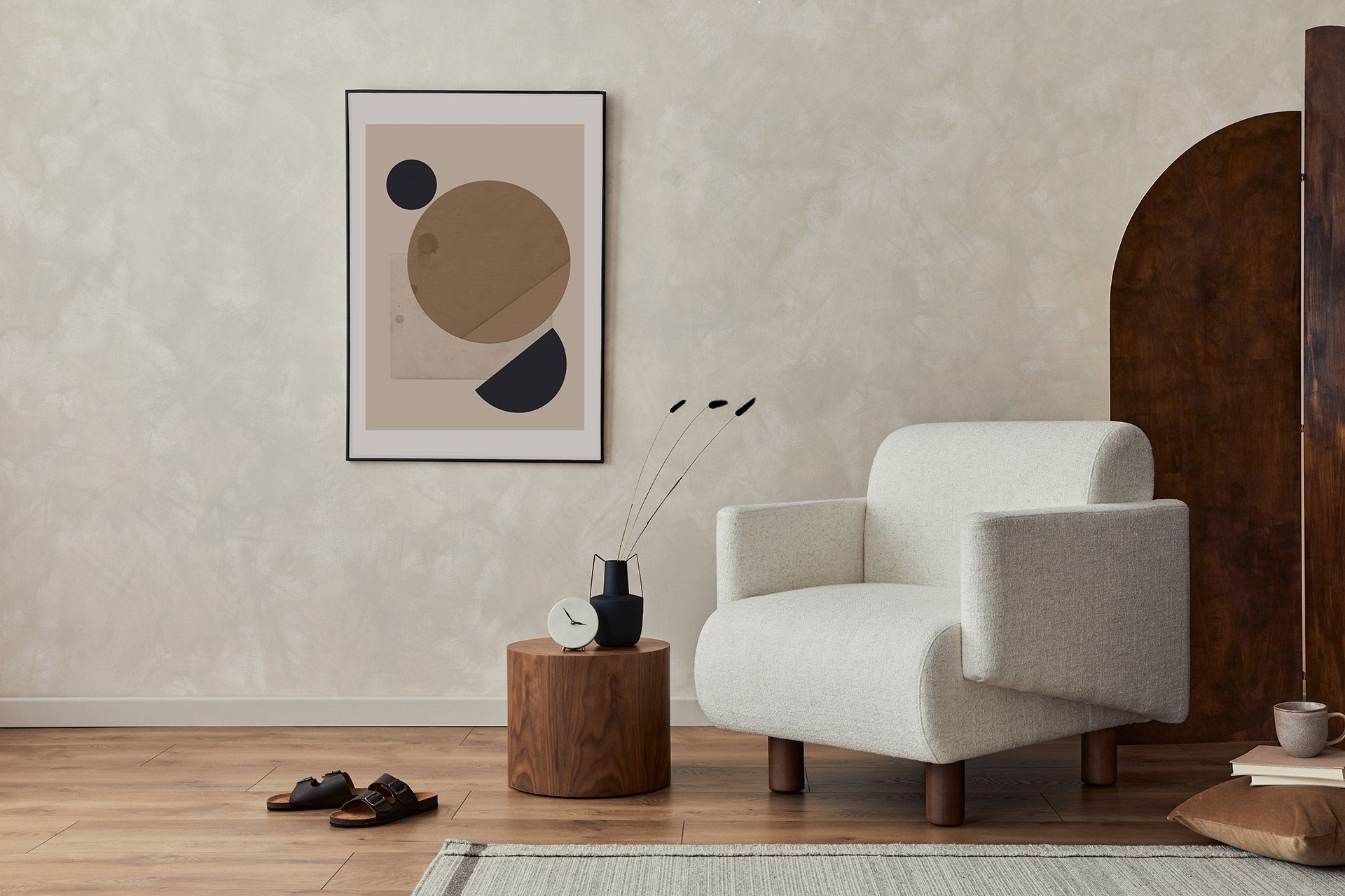 Minimal living room with white armchair, wall art, wooden side table, and sandals on a rug.
