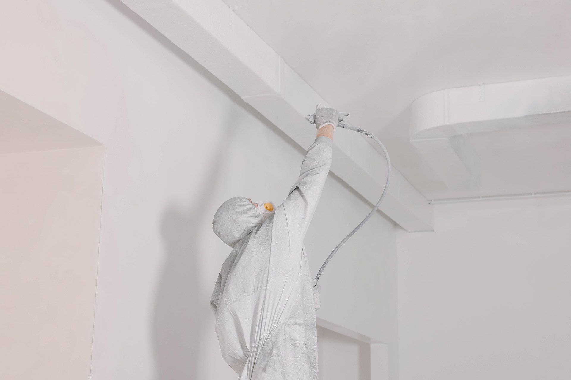 Worker in white protective suit painting a white ceiling with a roller extension