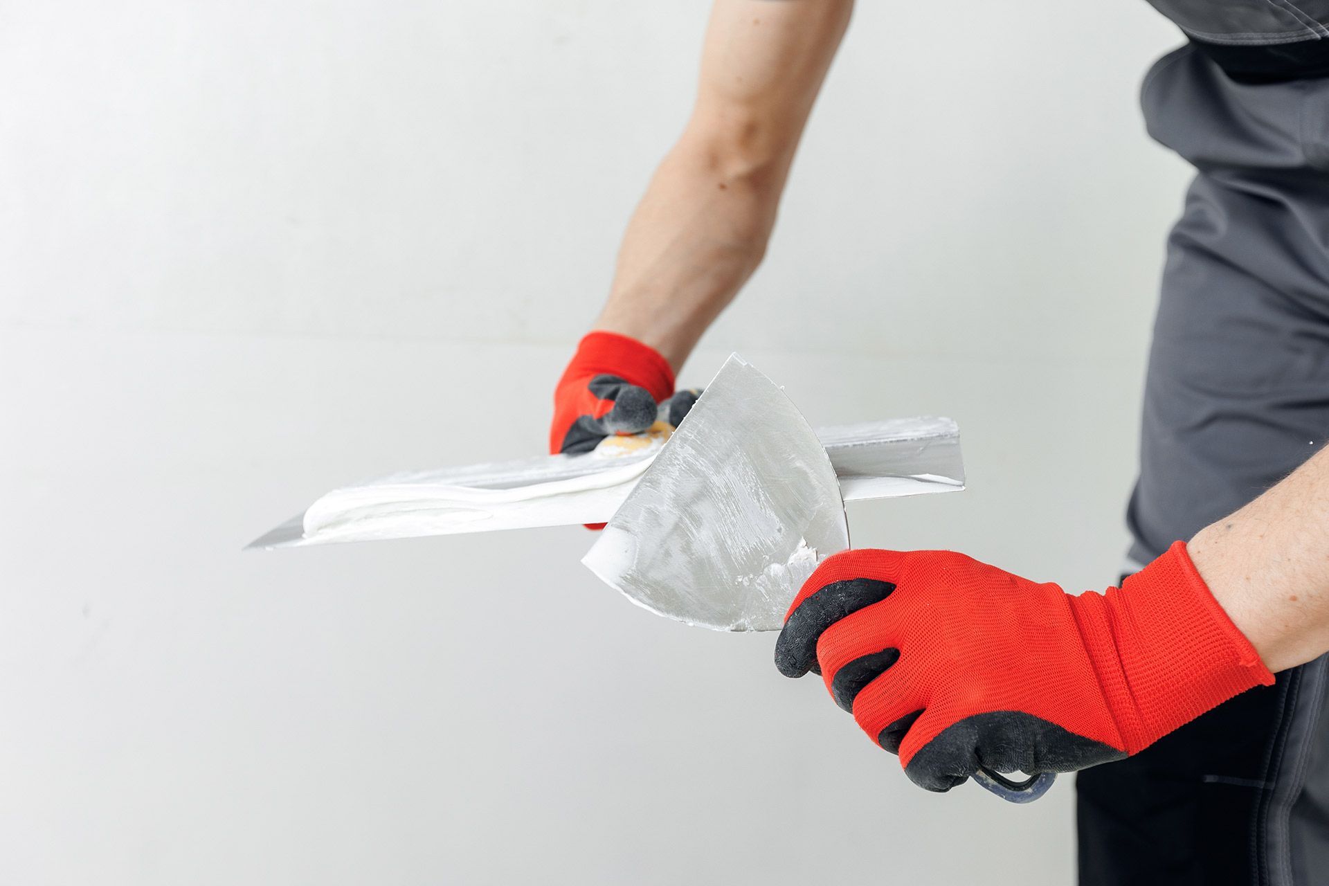 Person in red gloves applying white wall putty with a trowel on a wall